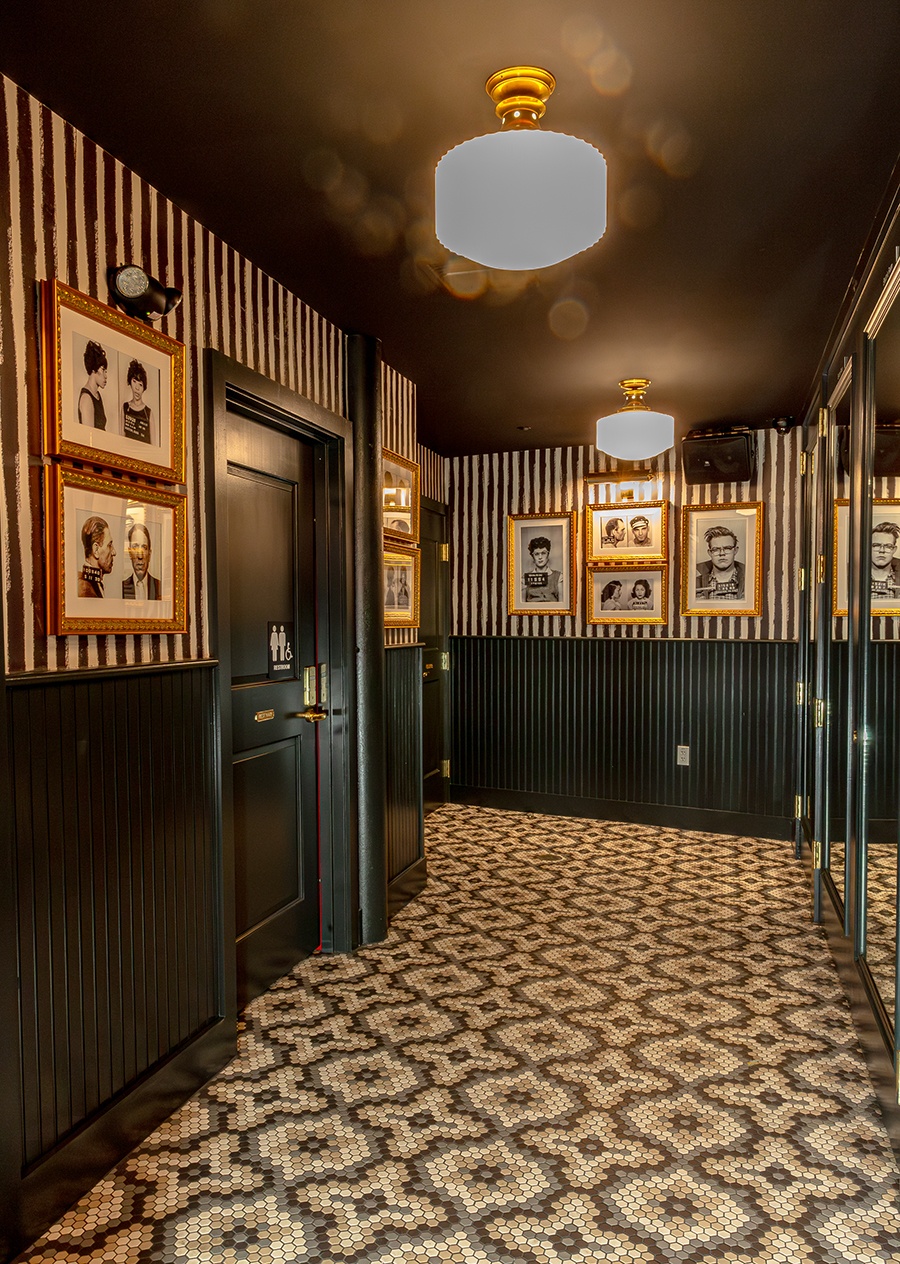 A tiled hallway has black-and-white striped walls with historical mugshots on display.