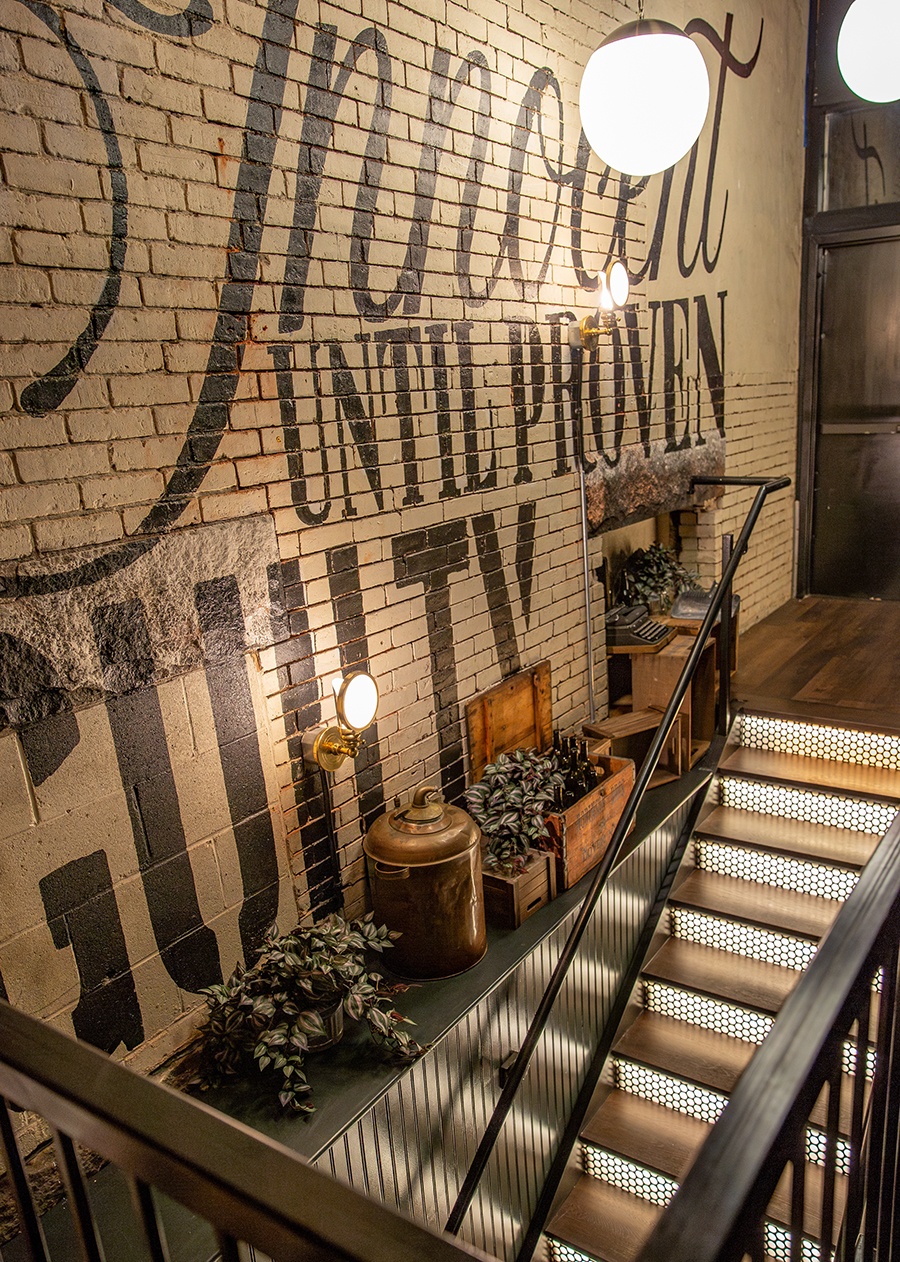 A white brick wall has large lettering that reads "innocent until proven guilty," next to an illuminated staircase heading down.