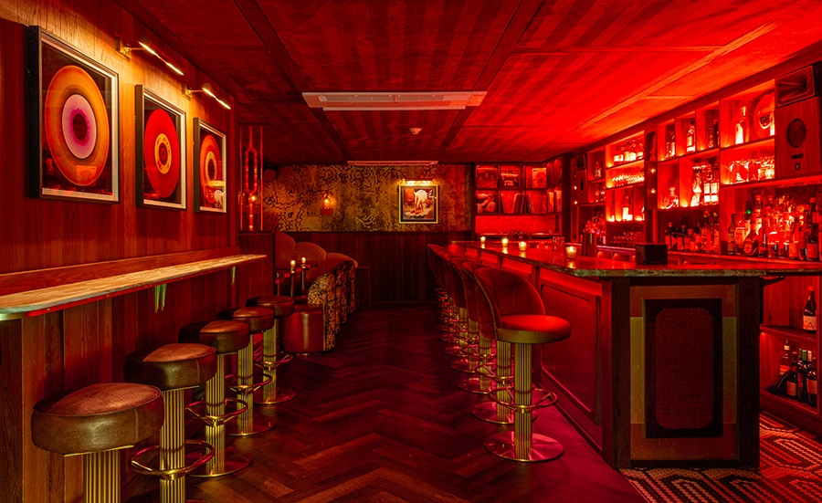 A dimly lit bar glows red and is decorated with records hanging on wood-paneled walls.