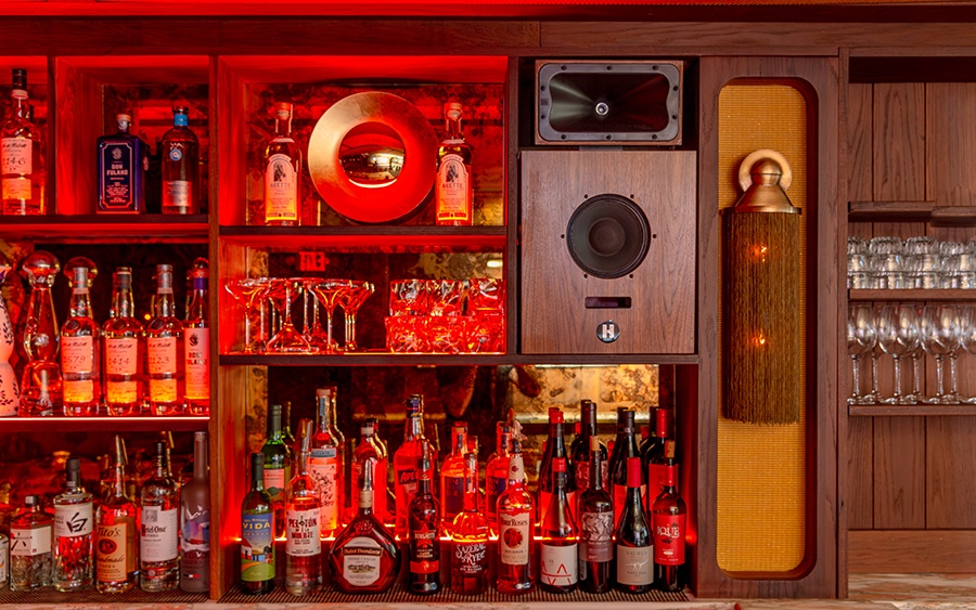 Bottles of liquor and speakers line the wall of a dimly lit lounge, glowing with red light.