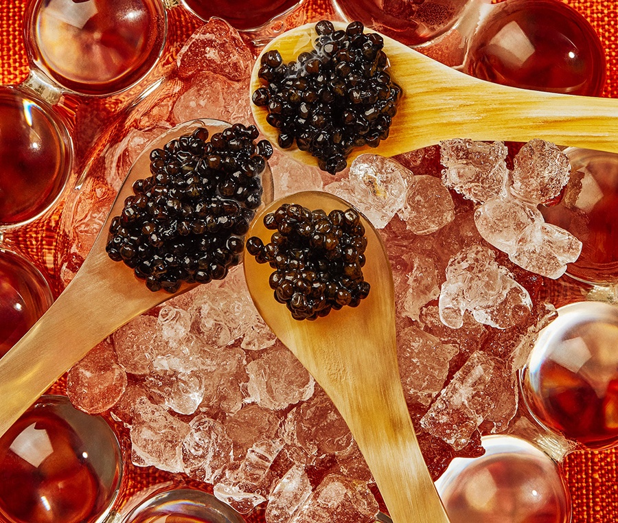 Three tiny wooden spoons perched over ice are full of caviar.