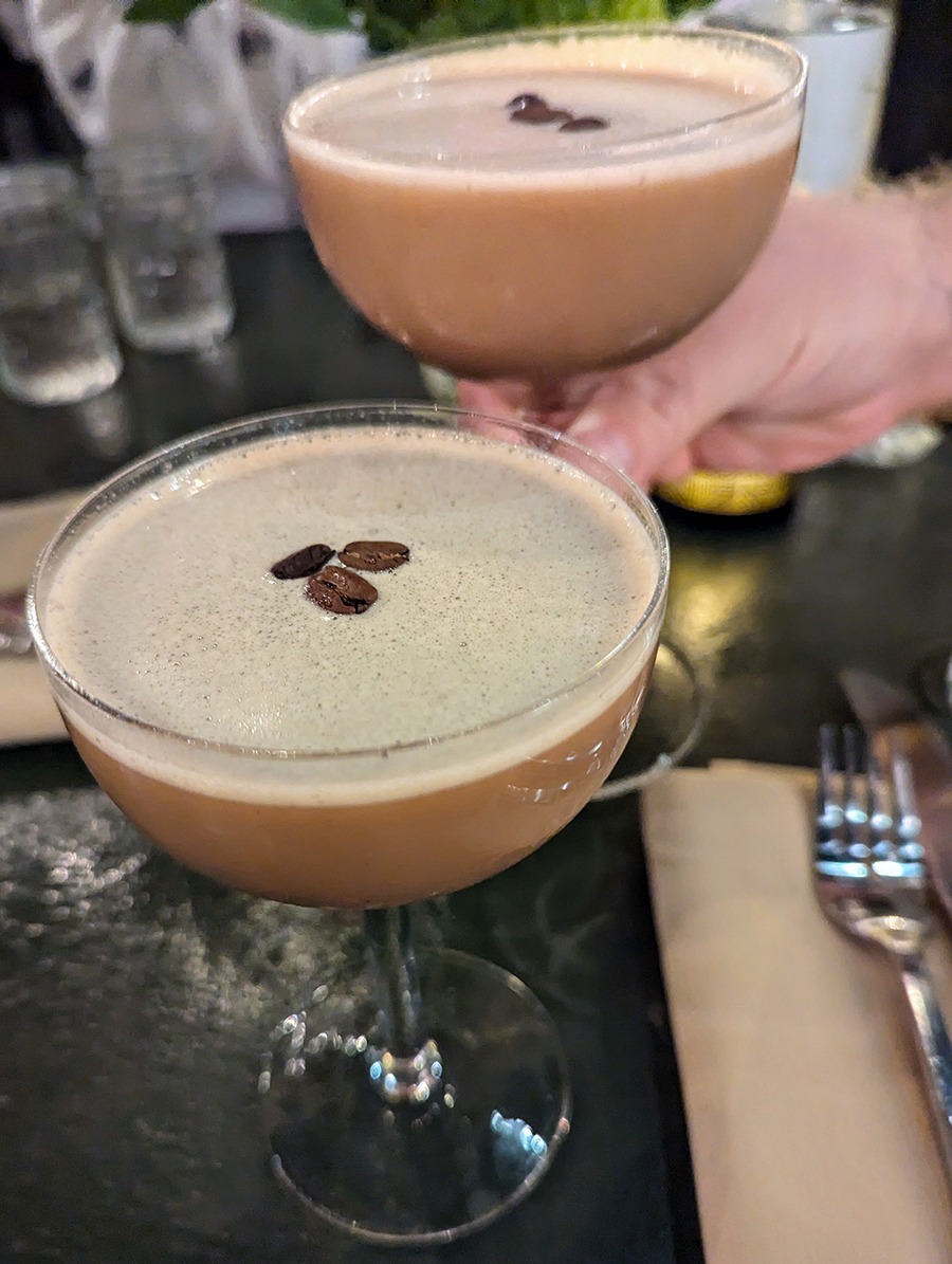 A pair of espresso martinis, garnished with coffee beans, sit on a table.