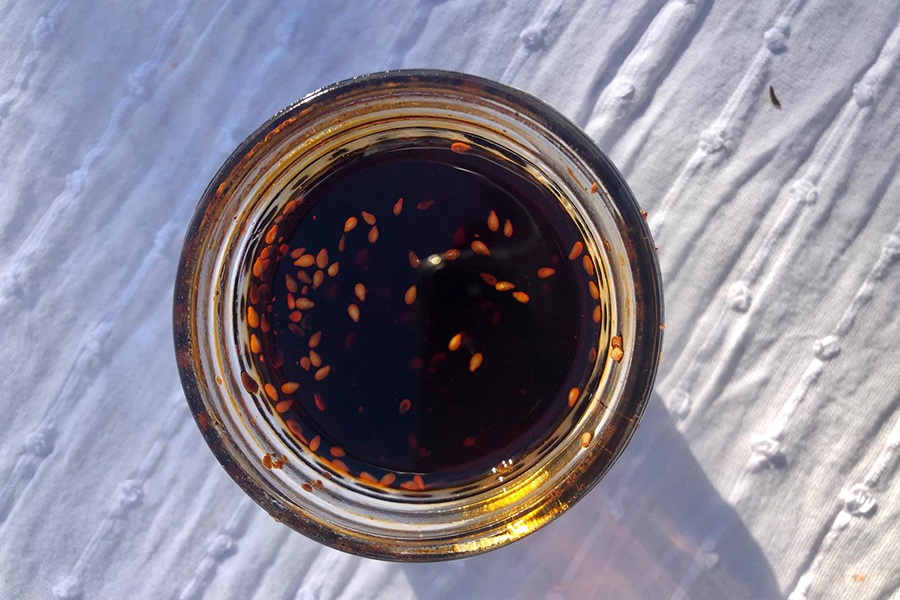 Overhead view of a jar of a dark red chili oil with sesame seeds.