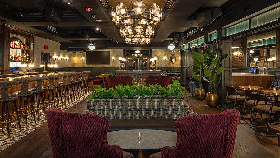 Empty restaurant interior with red velvet armchairs, khaki and gray banquettes, and a long bar.