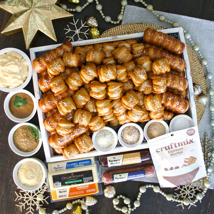 Overhead view of a box packed with soft pretzels and accoutrements, plus charcuterie.