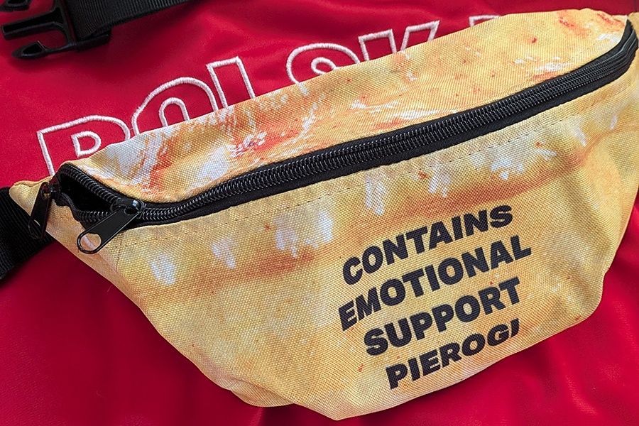 A light brown fanny pack has text reading "contains emotional support pierogi."