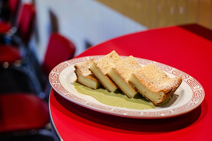 Slices of mochi sit in a pool of green sauce on a white and red plate.