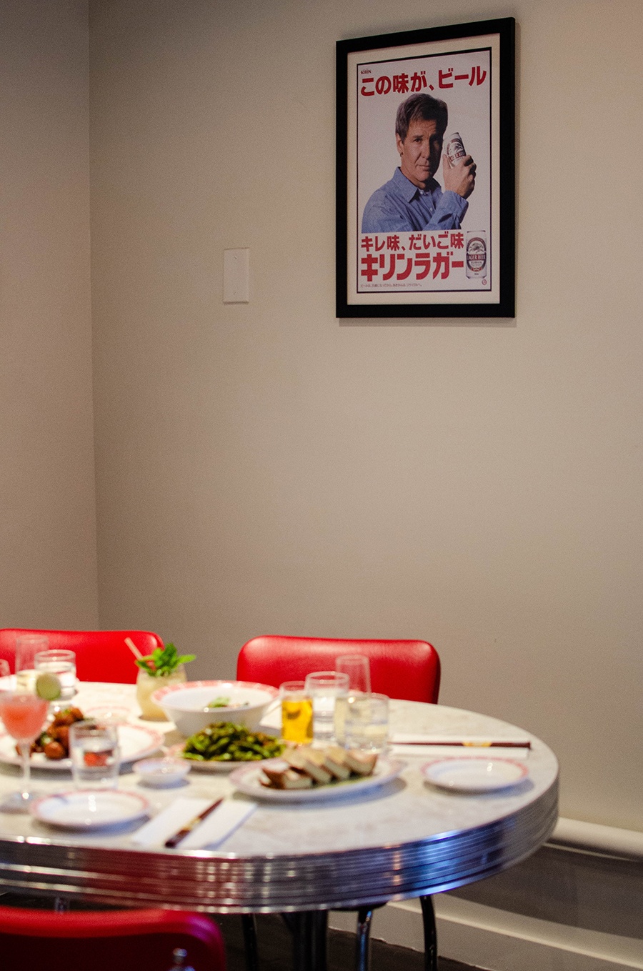 A framed image of Harrison Ford advertising a Japanese beer is hung above a restaurant table.