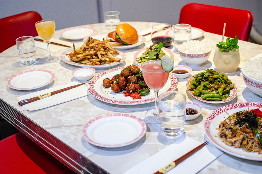 Edamame, noodles, fries, meatballs, cocktails, and more are displayed on a formica table with red chairs.