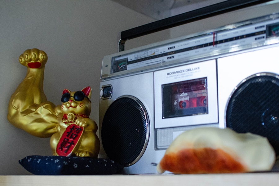 A boombox, gold cat statue, and dumpling decoration sit on a shelf.