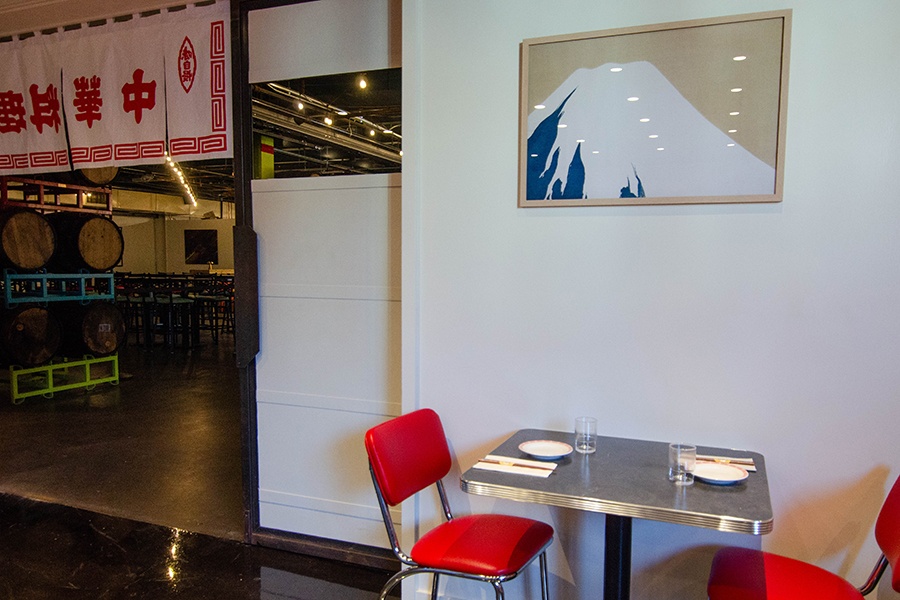 A restaurant interior features a simple art print of a snowy mountain and a banner with Japanese written on it.