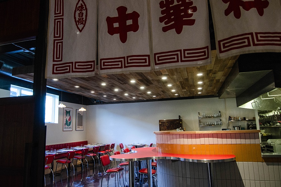 A restaurant interior features red chairs, white and yellow tiling, and a small, curvy, red standing bar.