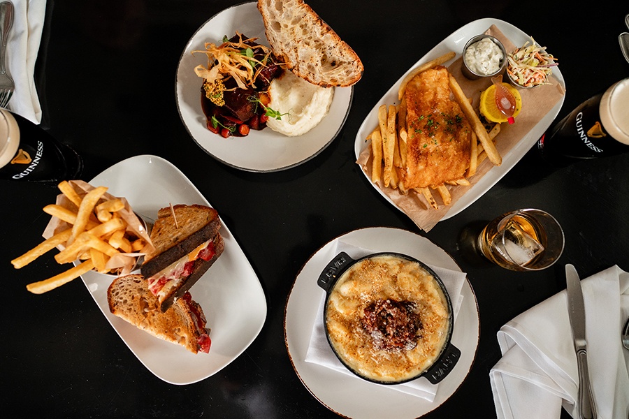 Overhead view of Irish-style dishes on a dark table, including a Reuben-like sandwich, fish and chips, and more.