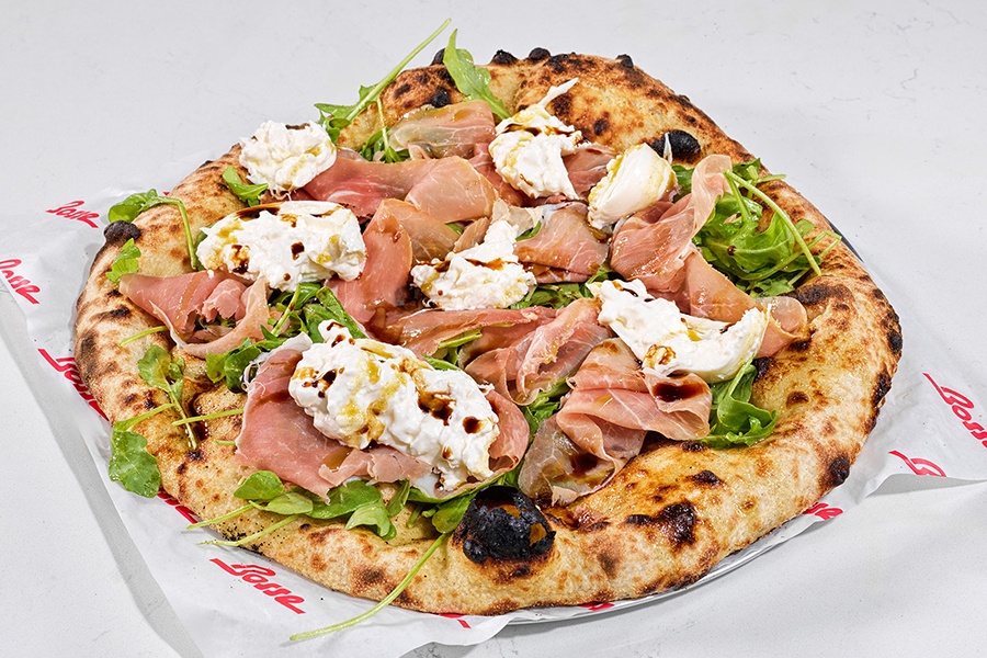 Pizza with a wood-fired, lightly charred crust is topped with big pieces of balsamic-drizzled burrata, prosciutto, and arugula.