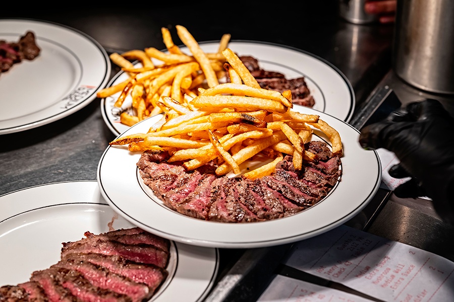 Plates of sliced steak with fries on a restaurant kitchen pass.