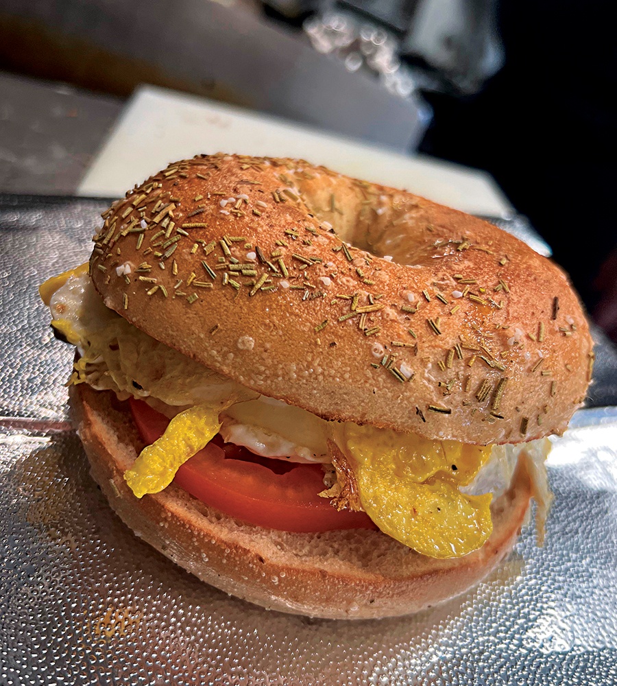 A bagel topped with rosemary and salt is stuffed with egg and tomato.