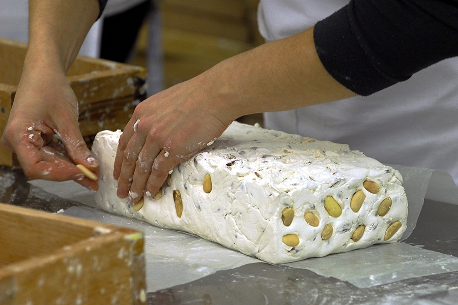 Hands put almond on a big white block of nougat.