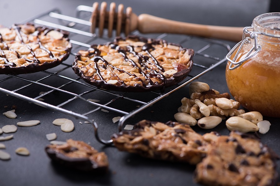 Chocolate-dipped nutty cookies are on a cooling rack next to a jar of honey.