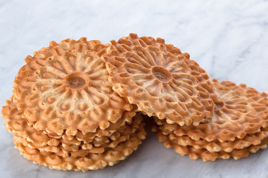 Italian waffle coookies are stacked on white marble.