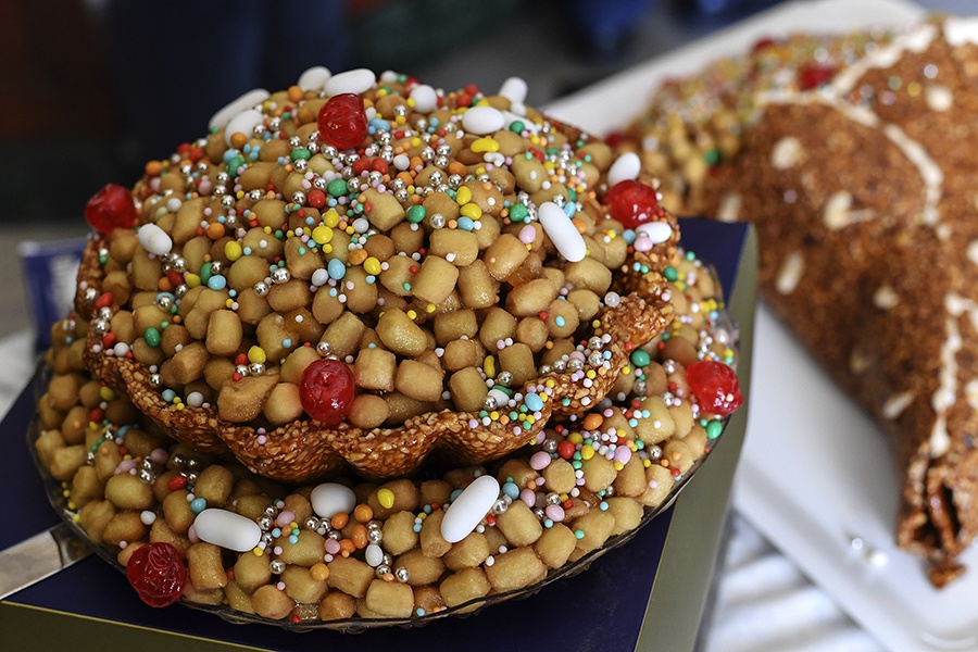 Small fried dough balls, shiny with a honey coating, are piled up and garnished with colorful sprinkles.