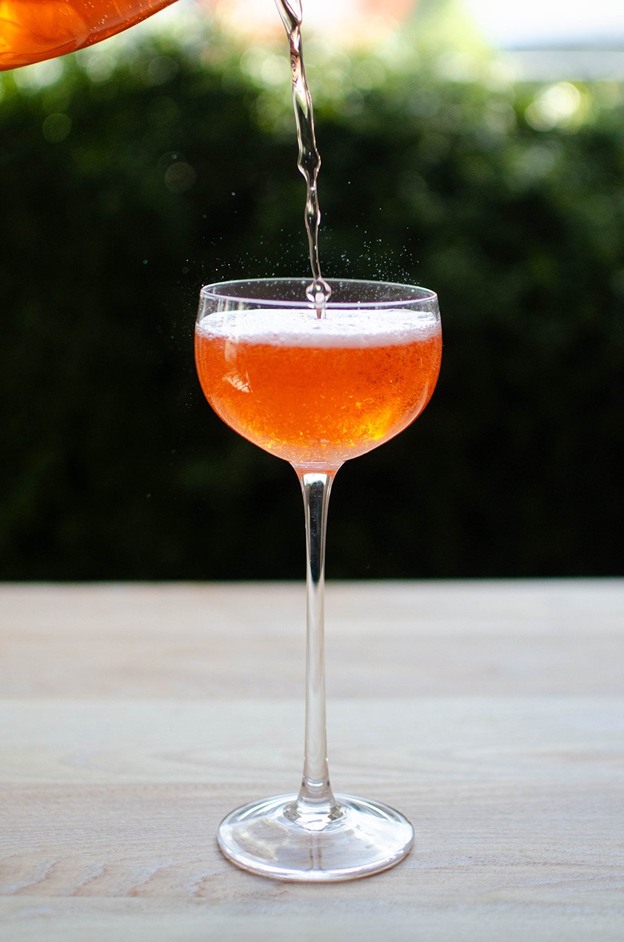 A fizzy orange cocktail is poured into a coupe glass, bubbles jumping up from the surface.