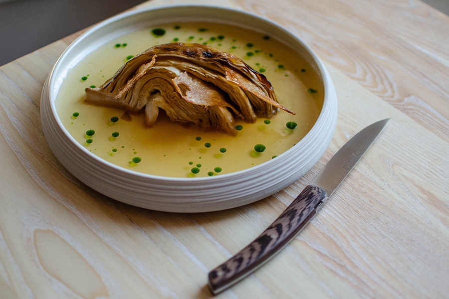 Part of a head of cabbage, smoked and beige, sits in a pool of yellowish broth dotted with green oil.