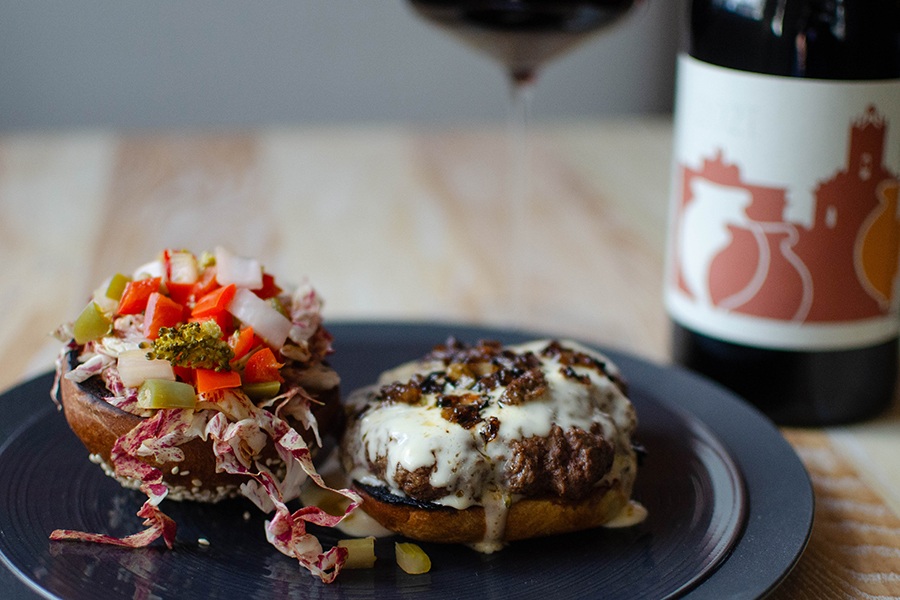 A cheeseburger is presented in two halves, with the top of the bun topped with giardiniera.