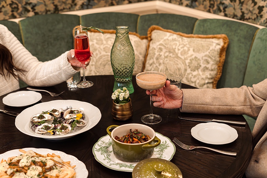 Hands reach to pick up holiday cocktails from an elegant table full of winter food, including poutine and beef bourguignon.