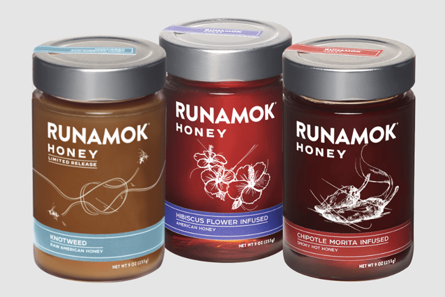 Three glass jars of honey from the brand Runamok, in different flavors, are isolated on a white background.