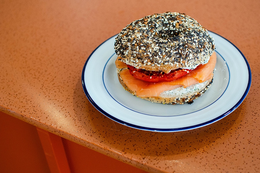 Lox, cream cheese, and tomato on an everything bagel on an orange counter.