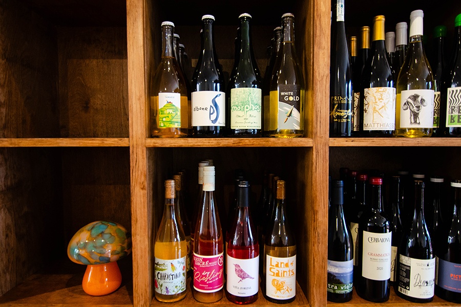 Bottles of wine fill wooden shelves, alongside a decorative glass mushroom.