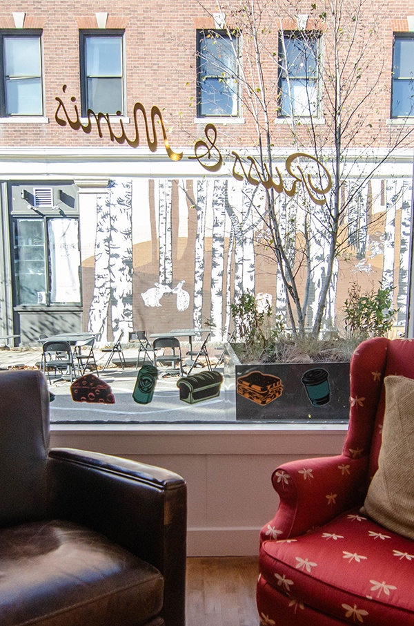 Two mismatched armchairs sit in the window of a market with Russ & Mimi's written in gold script. A birch tree mural is visible through the window.