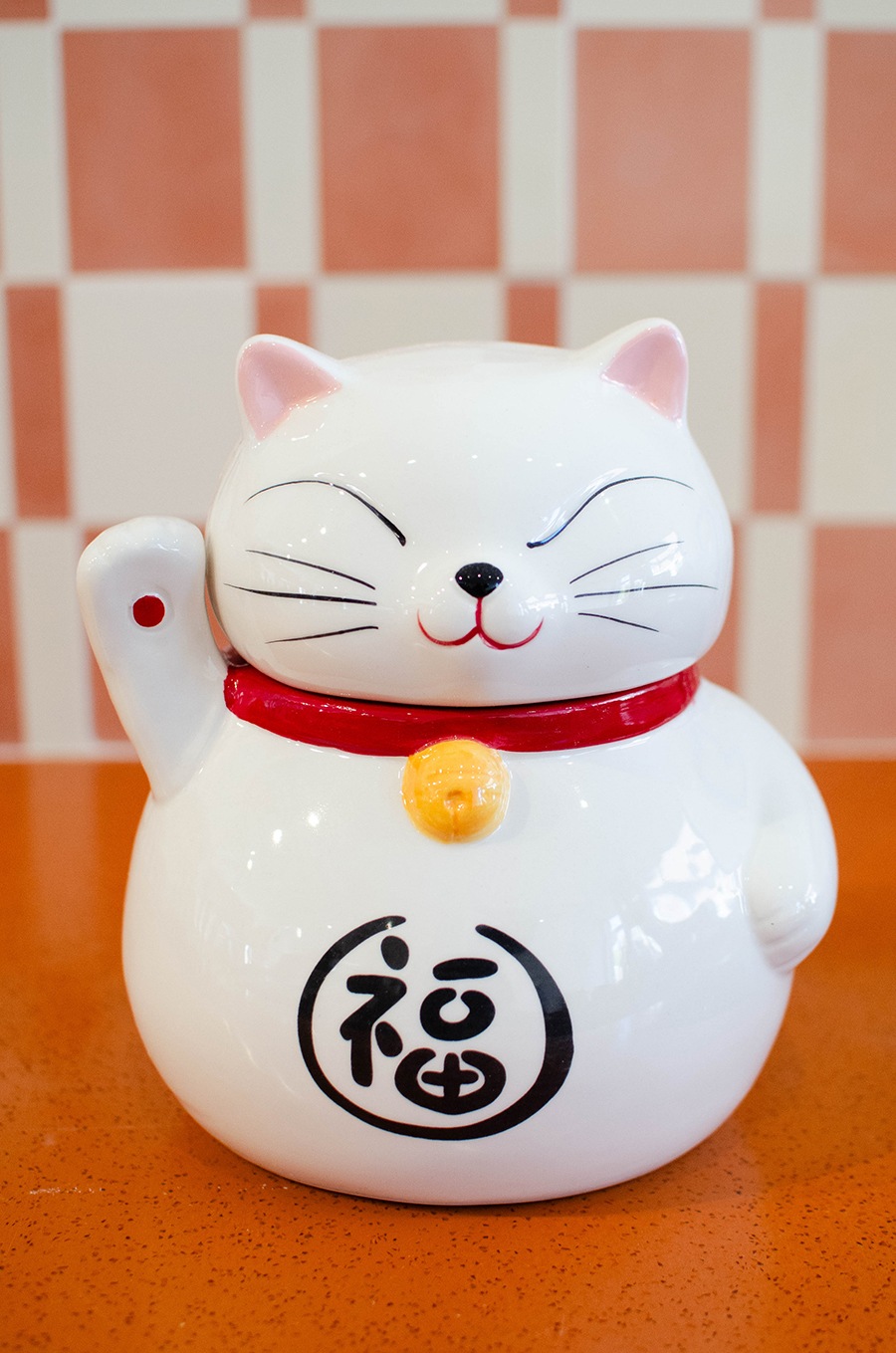 A smiling white cat figurine waves.