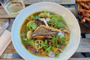 Overhead view of a brothy seafood dish with lots of herbs and vegetables, served on a picnic table.