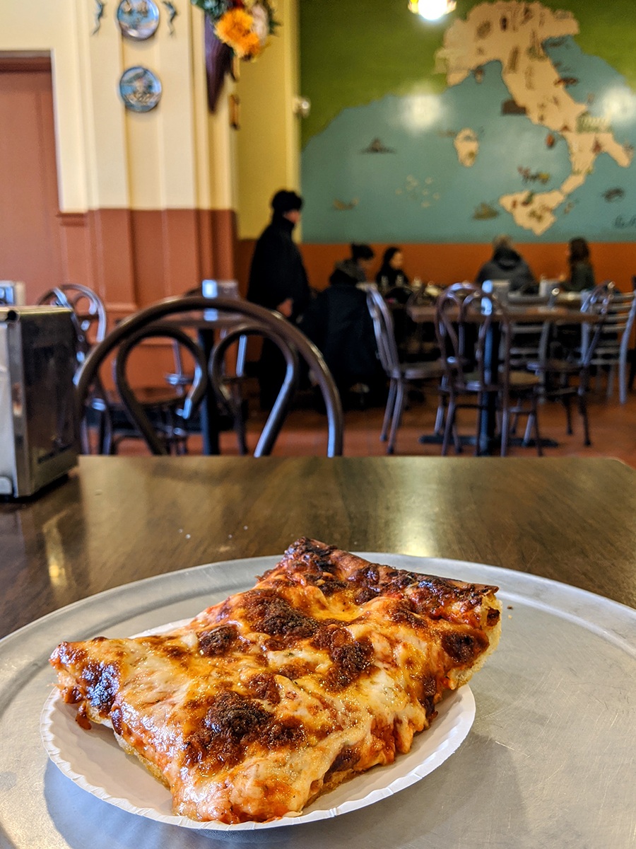 A well-browned rectangle of Sicilian pizza in a cafeteria-like restaurant.