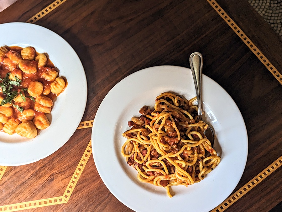 Overhead view of two pasta dishes sitting on a wooden table.