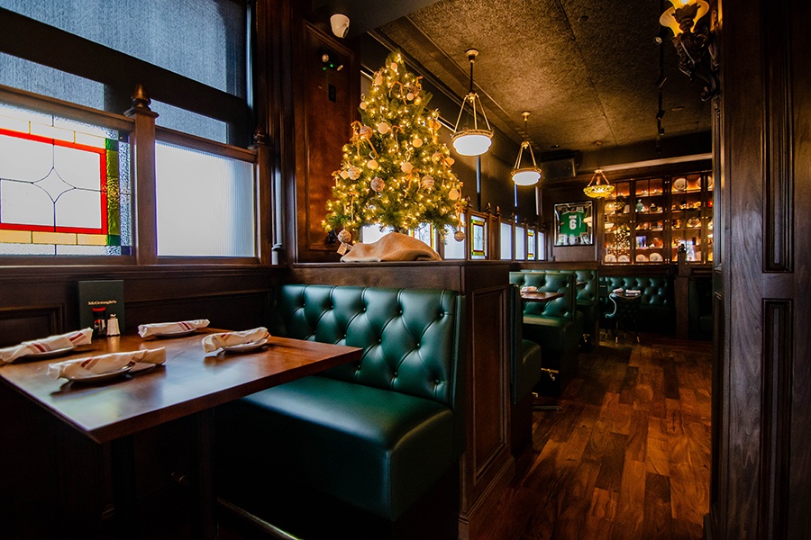 Green booths, dark wood, and stained glass decorate an Irish pub, plus a small Christmas tree.