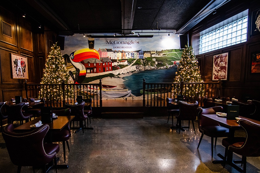 A restaurant interior features a large colorful mural with the Guinness toucan and a seaside village.