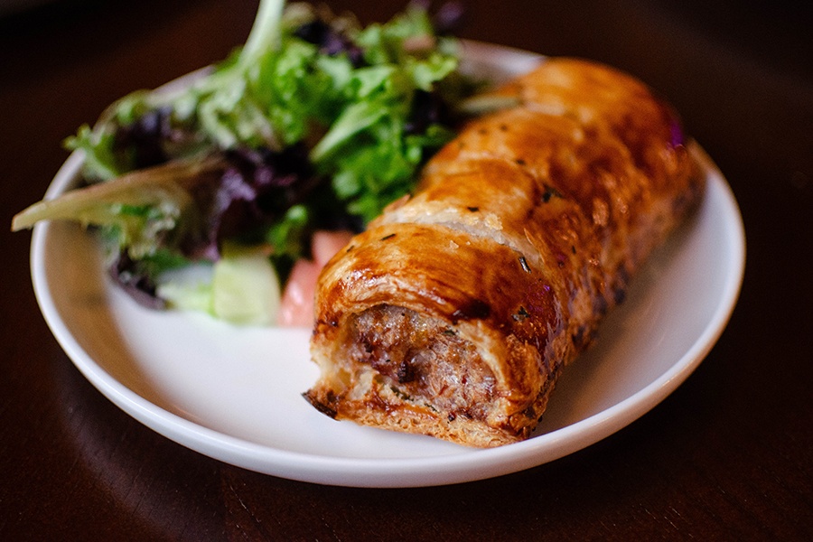 Puff-pastry-wrapped sausage is accompanied by a simple salad on a small white plate.