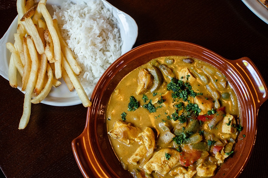 Overhead view of diced chicken and peppers in a yellow curry, accompanied by thin fries and white rice.