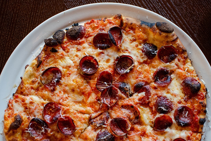 Overhead view of a thin pizza with slight charred crusy and browned pepperoni cups.