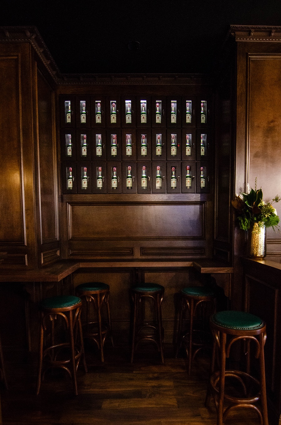 Whiskey bottles are displayed in lockers on a dark wooden wall in an Irish pub.