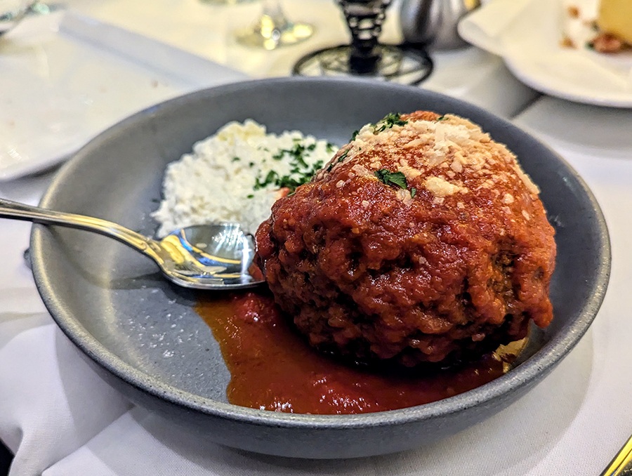 A big meatball sits in a pool of tomato sauce with a side of ricotta.