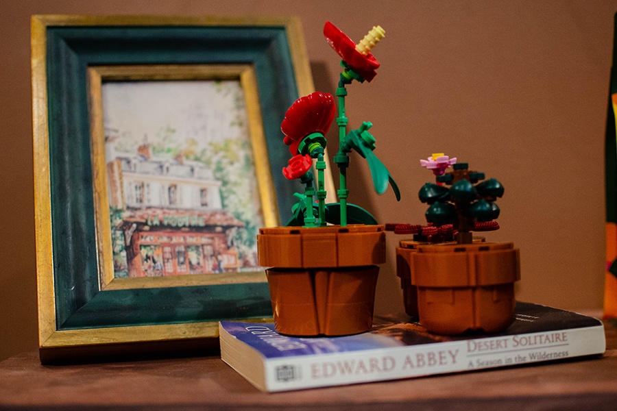 Small potted plants made out of lego-like bricks sit in front of a small painting of the exterior of a cafe.