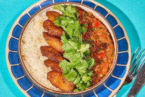 Overhead view of ropa vieja - rice, plantains, and a beefy stew - on a blue plate on a turquoise background.