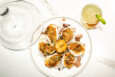 Overhead view of six cooked oysters with a cheesy topping and a grilled lemon half in the middle, next to a glass cloche and a light green cocktail.