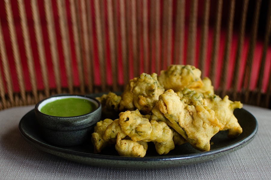 Crispy pakora sit on a dark plate next to a thick green sauce.