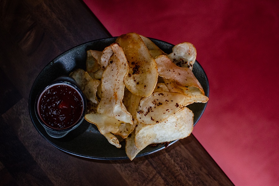 Overhead view of a plate of spiced potato chips with a dark red dipping sauce.