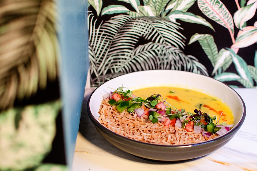 A yellow curry-like sauce is plated with basmati rice and a bit of salad, presented in front of tropical wallpaper.