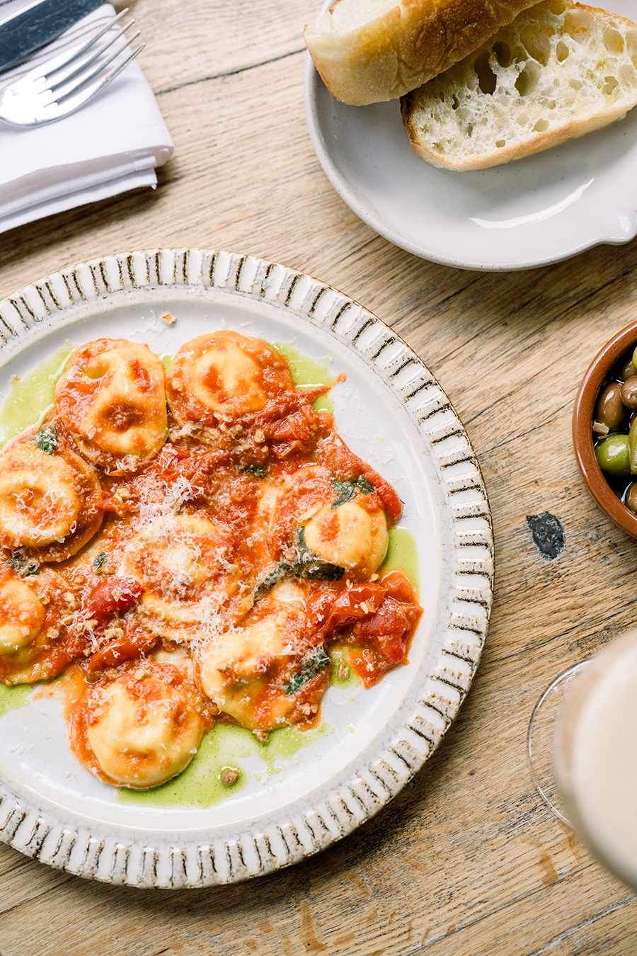 Overhead view of ravioli and bread on a light wooden table.